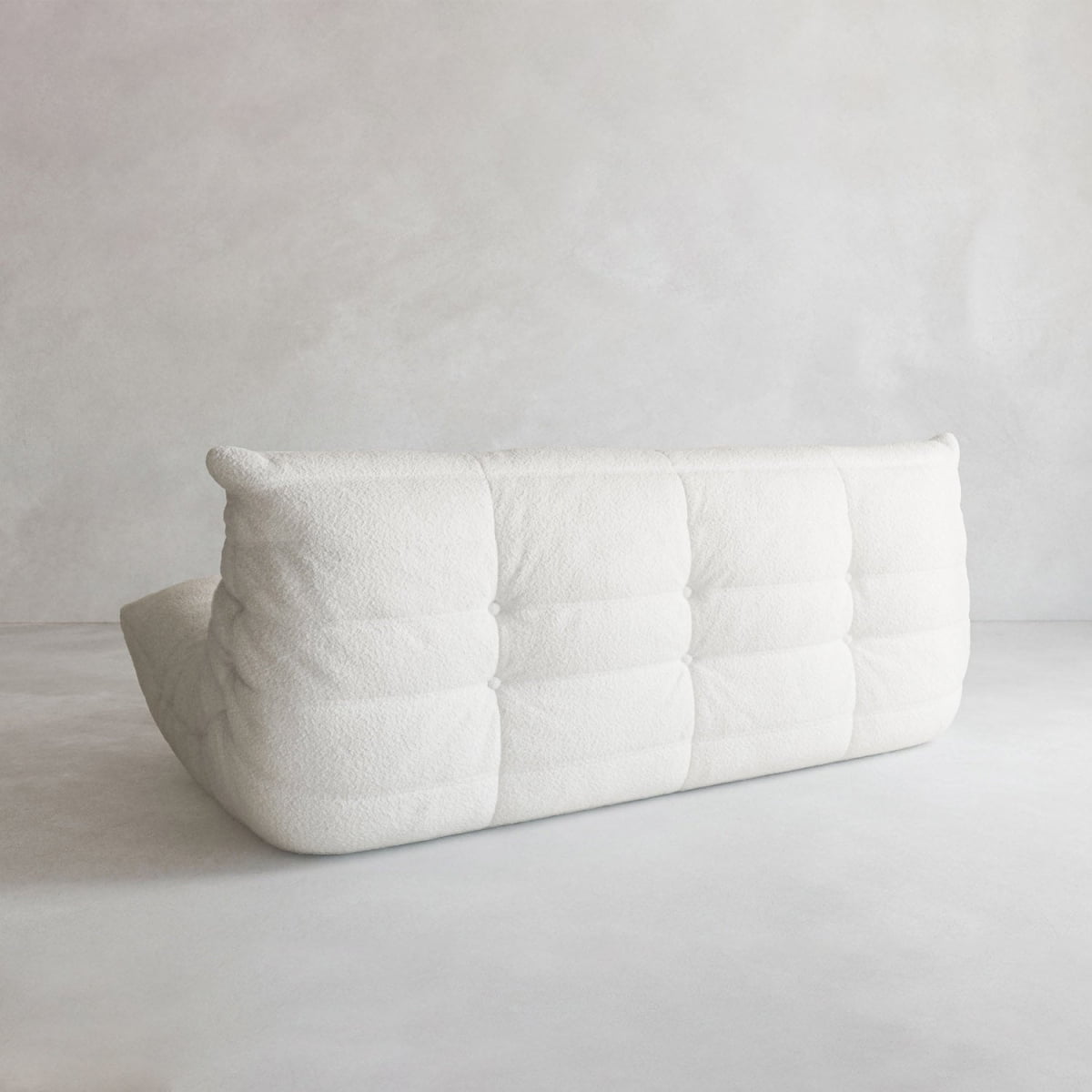 The Rolo Lounge Three Seater—a modern white tufted sofa with soft, textured upholstery and mid-century design touches—is shown from behind on a light gray floor against a plain, light background.