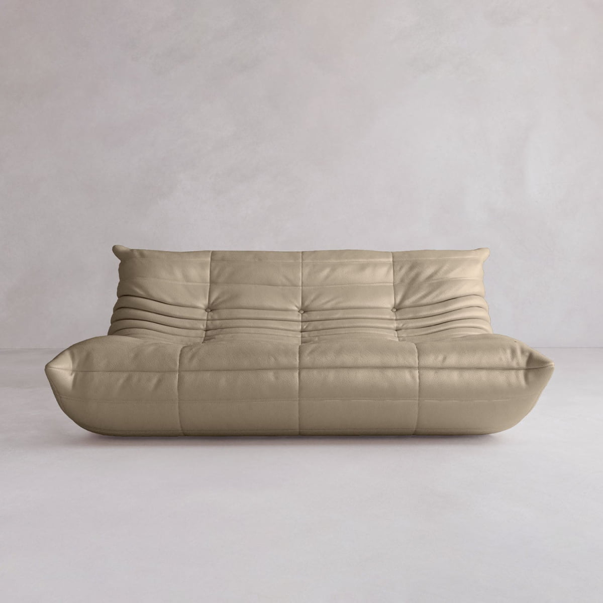 The Rolo Lounge Three Seater is a modern, beige, armless leather sofa with a low back and deep cushioned seat in subtle mid-century style, set against a plain light gray wall and floor.