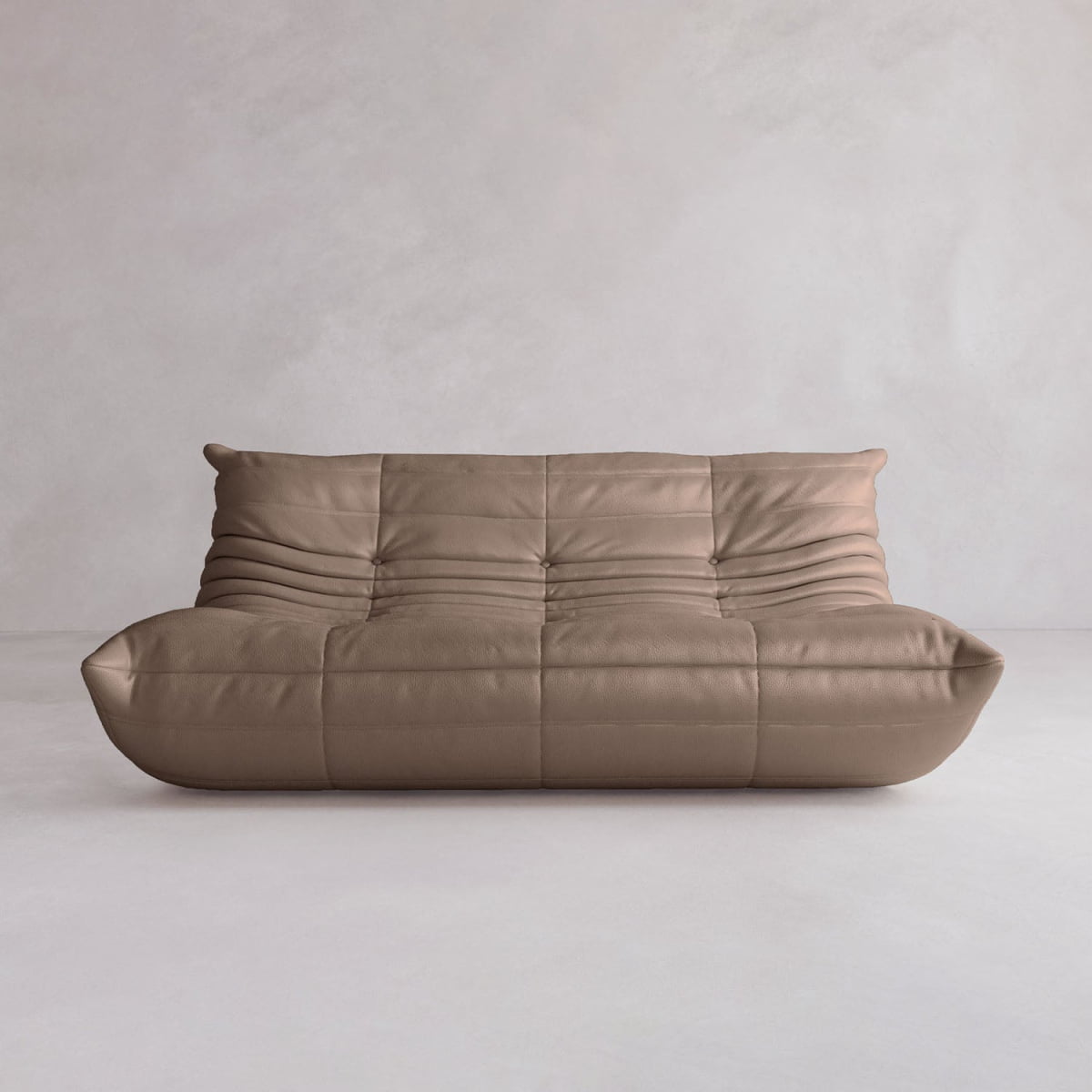 The Rolo Lounge Three Seater, a modern low-profile brown leather sofa with tufted plush design and subtle mid-century style, sits on a light floor against a plain light grey wall.