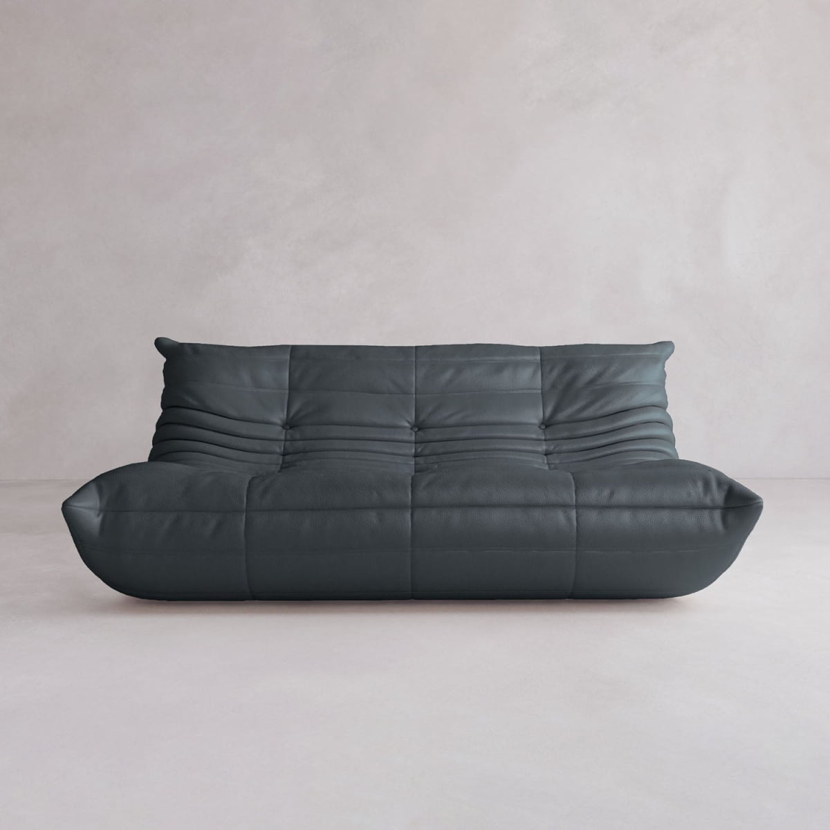 The Rolo Lounge Three Seater is a modern, armless sofa in dark gray with a low profile and plush tufted cushions, inspired by mid-century design, set against a plain light gray wall and floor.