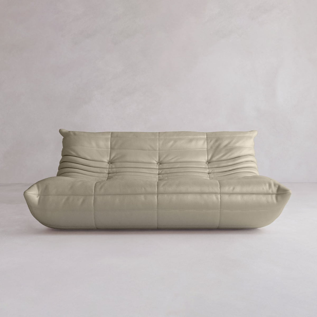 The Rolo Lounge Three Seater, a modern, low-profile beige sofa with tufted curved cushions and minimalist mid-century design, sits against a light textured wall in an empty room.