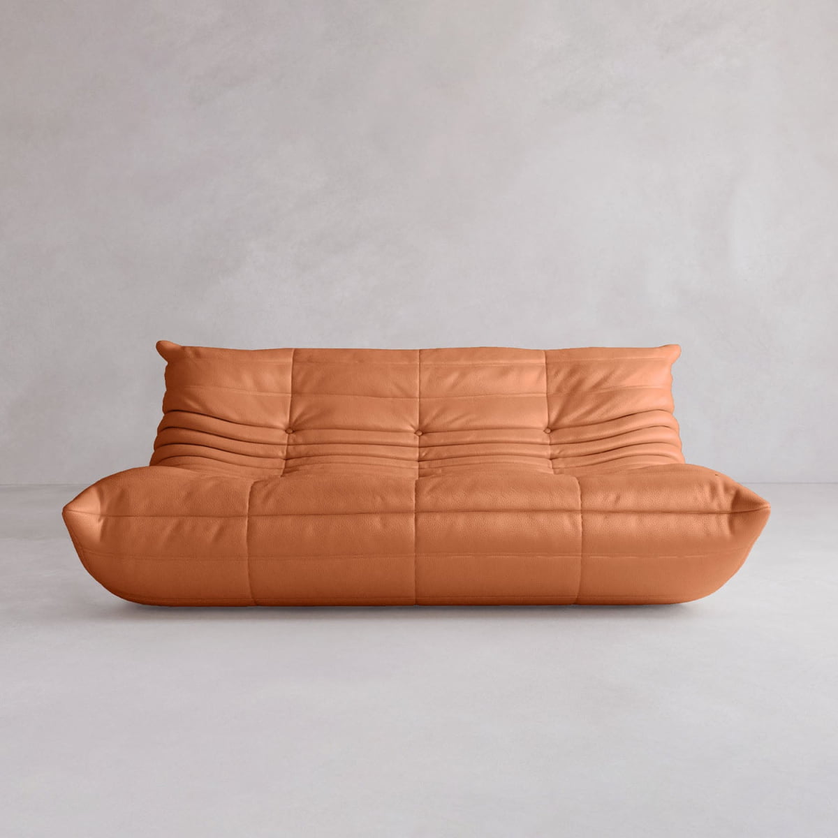 The Rolo Lounge Three Seater is a modern, low-profile tan leather sofa with a tufted, softly wrinkled surface in a mid-century design, shown against a plain light gray wall and floor.