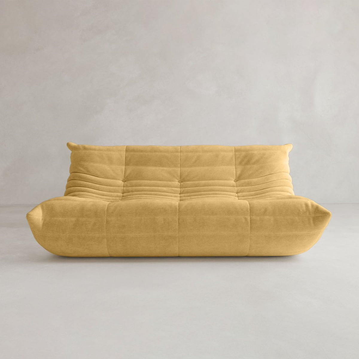 The Rolo Lounge Three Seater, a mustard yellow modern armless sofa with tufted upholstery and a low profile, evoking mid-century style, sits against a plain light gray wall and floor.