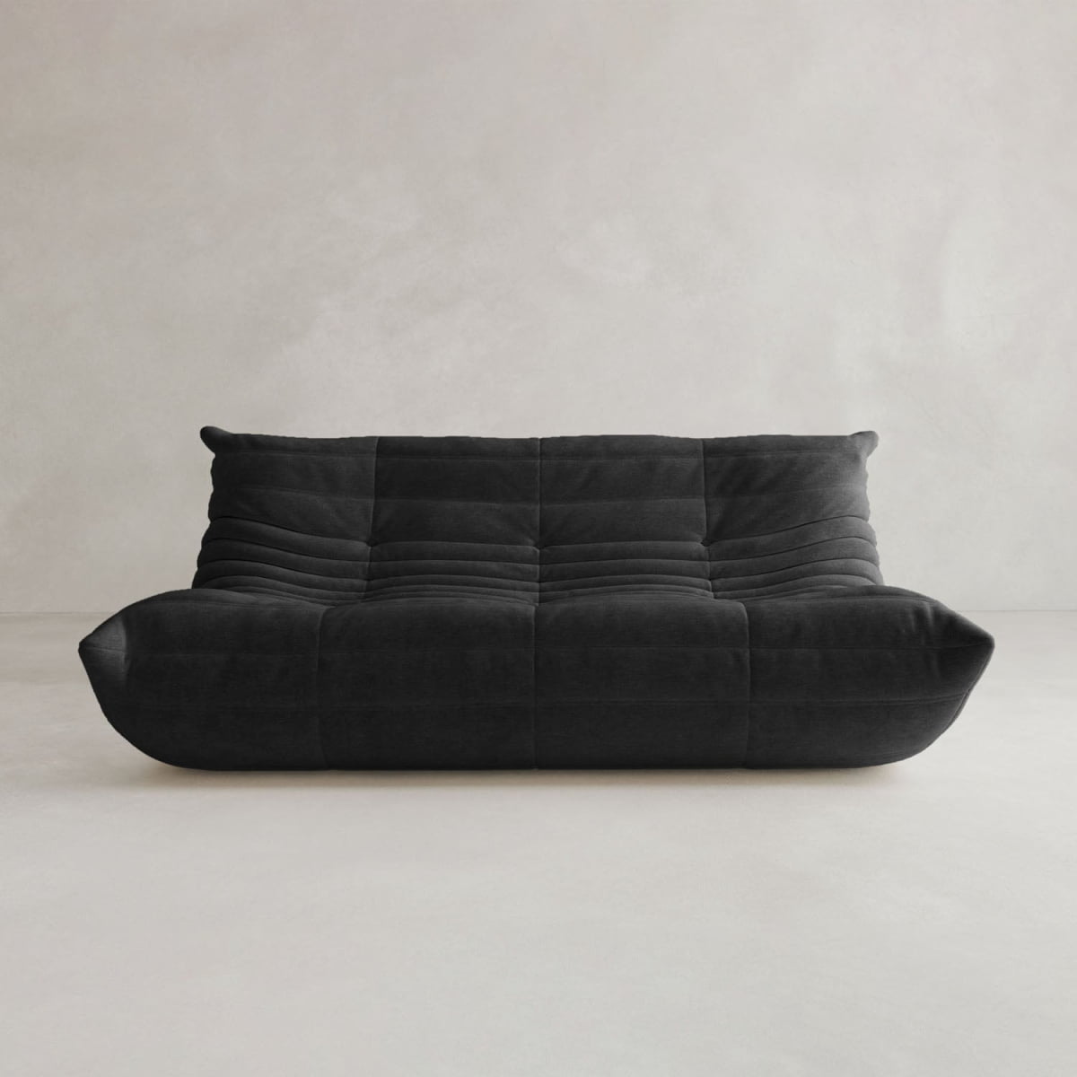 The Rolo Lounge Three Seater, a modern low-profile black sofa with tufted cushions inspired by mid-century design, is set against a light gray minimalist background.