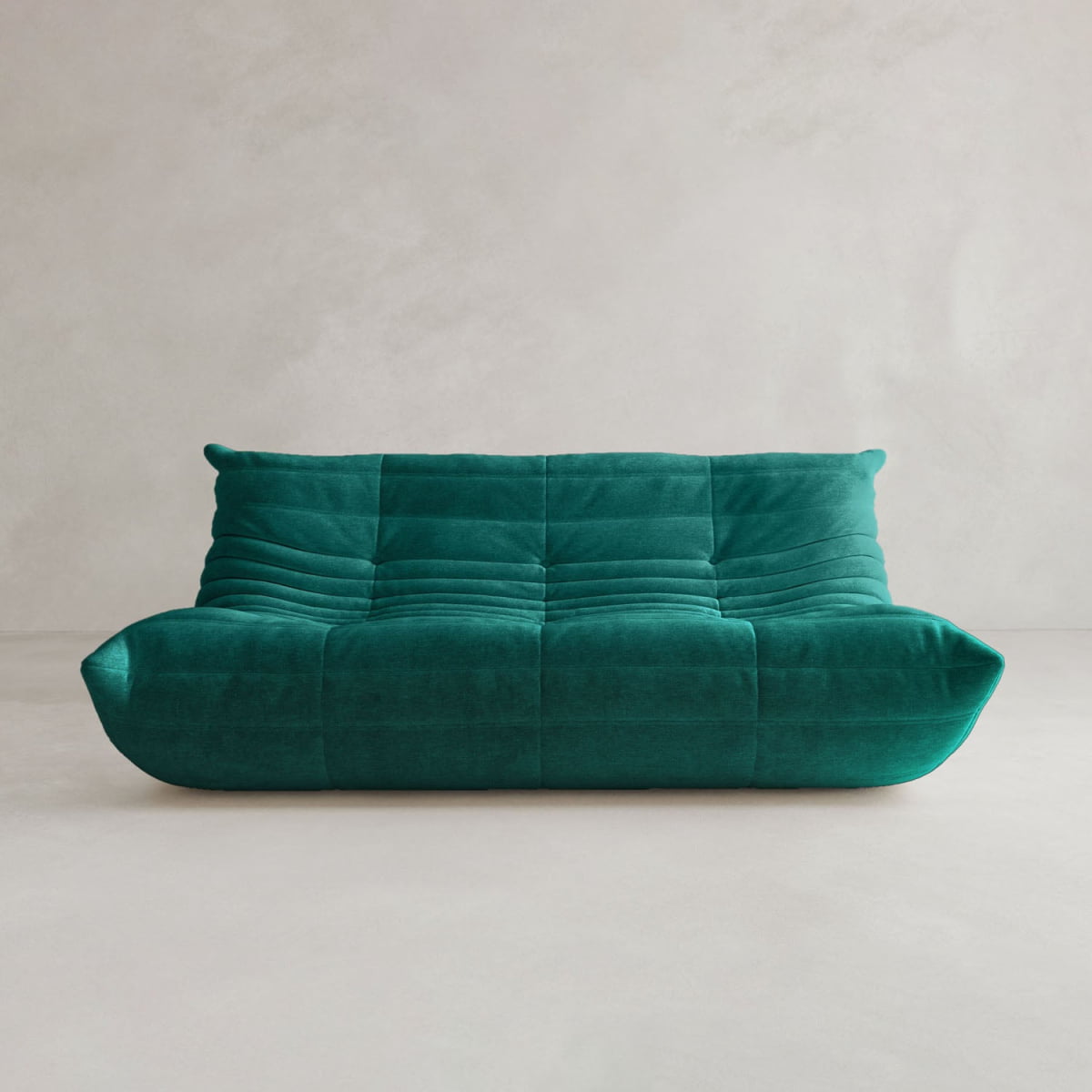 The Rolo Lounge Three Seater is a modern teal velvet sofa with a low profile, tufted seat and back, and soft rounded edges that showcase mid-century design, set against a plain light-colored wall and floor.