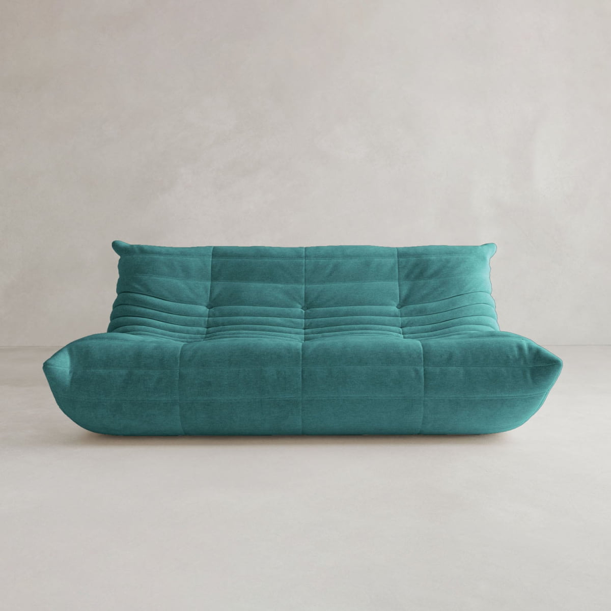 The Rolo Lounge Three Seater, a modern teal sofa with plush, quilted upholstery and a low backrest inspired by mid-century design, sits against a light-colored wall in a minimalistic room.