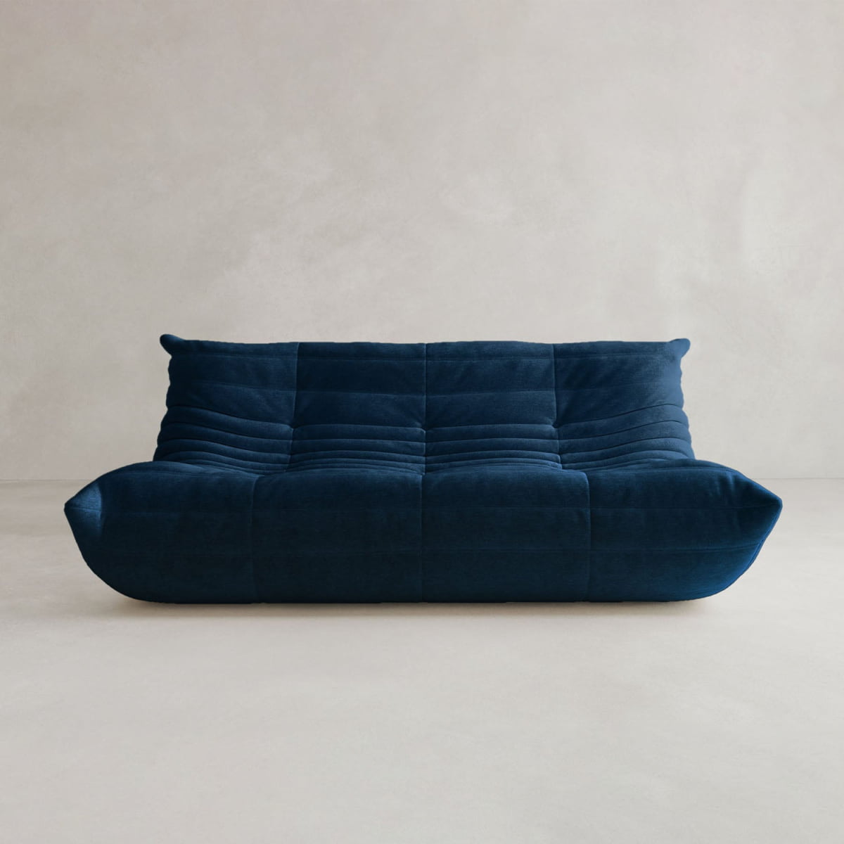 The Rolo Lounge Three Seater, a modern deep blue, armless sofa with a low back and tufted plush cushions, adds mid-century flair to a light floor and neutral backdrop.