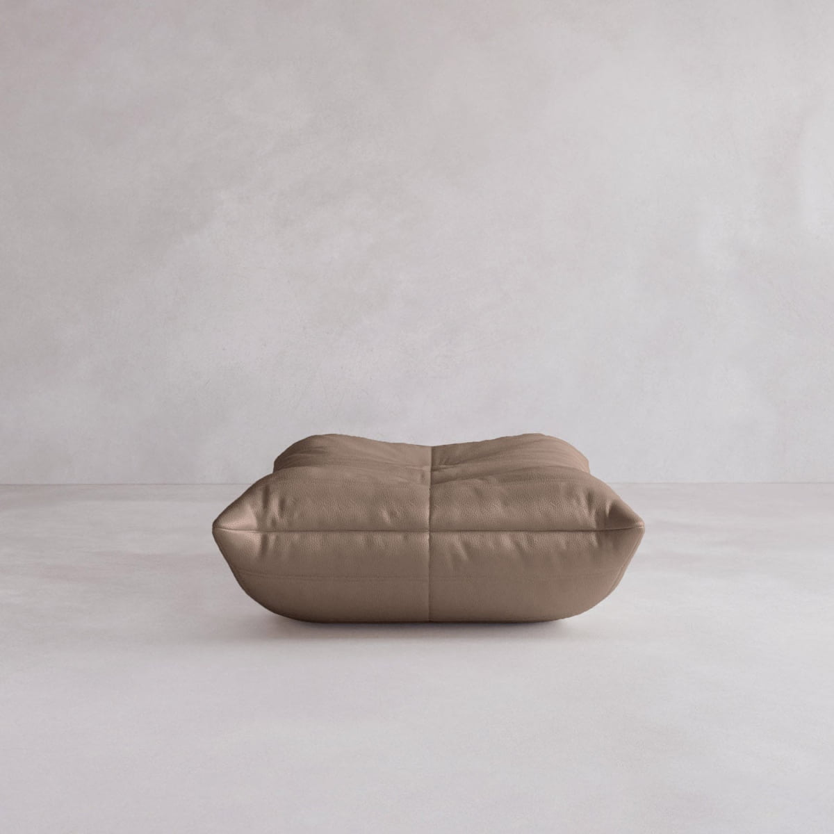 The Rolo Ottoman, a large square floor cushion with a cushioned top and visible seams, sits on a light gray floor against a plain wall. Its plush appearance makes it a versatile addition to any modern living space.