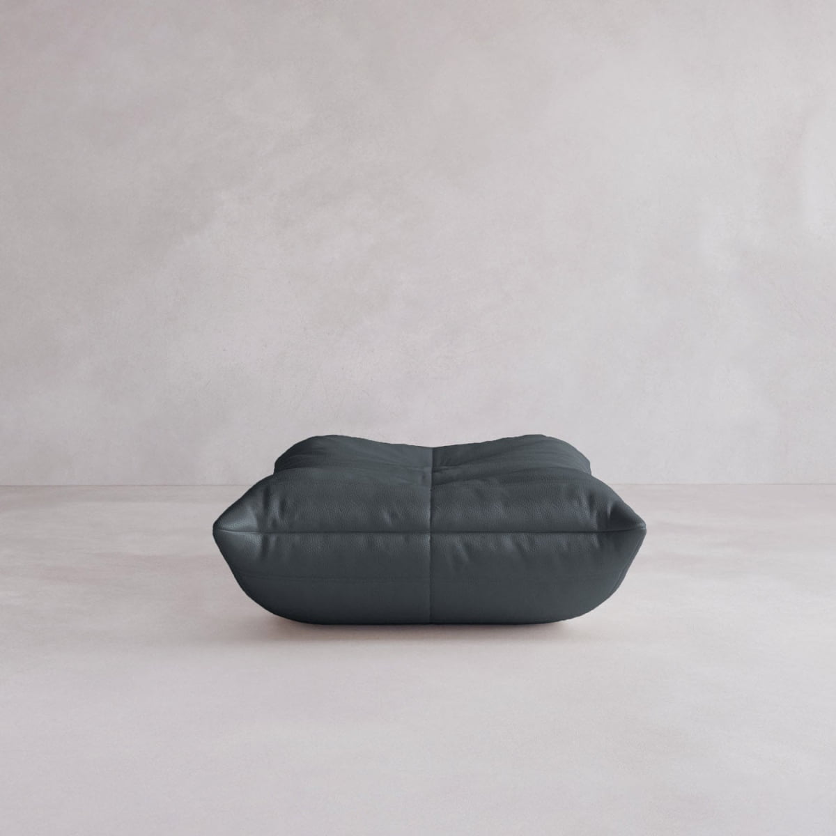 The Rolo Ottoman, a dark gray rectangular floor pouf with visible seams and a cushioned top, adds sleek style and comfort to any room. Its plush design makes it versatile for seating or decor in modern spaces.