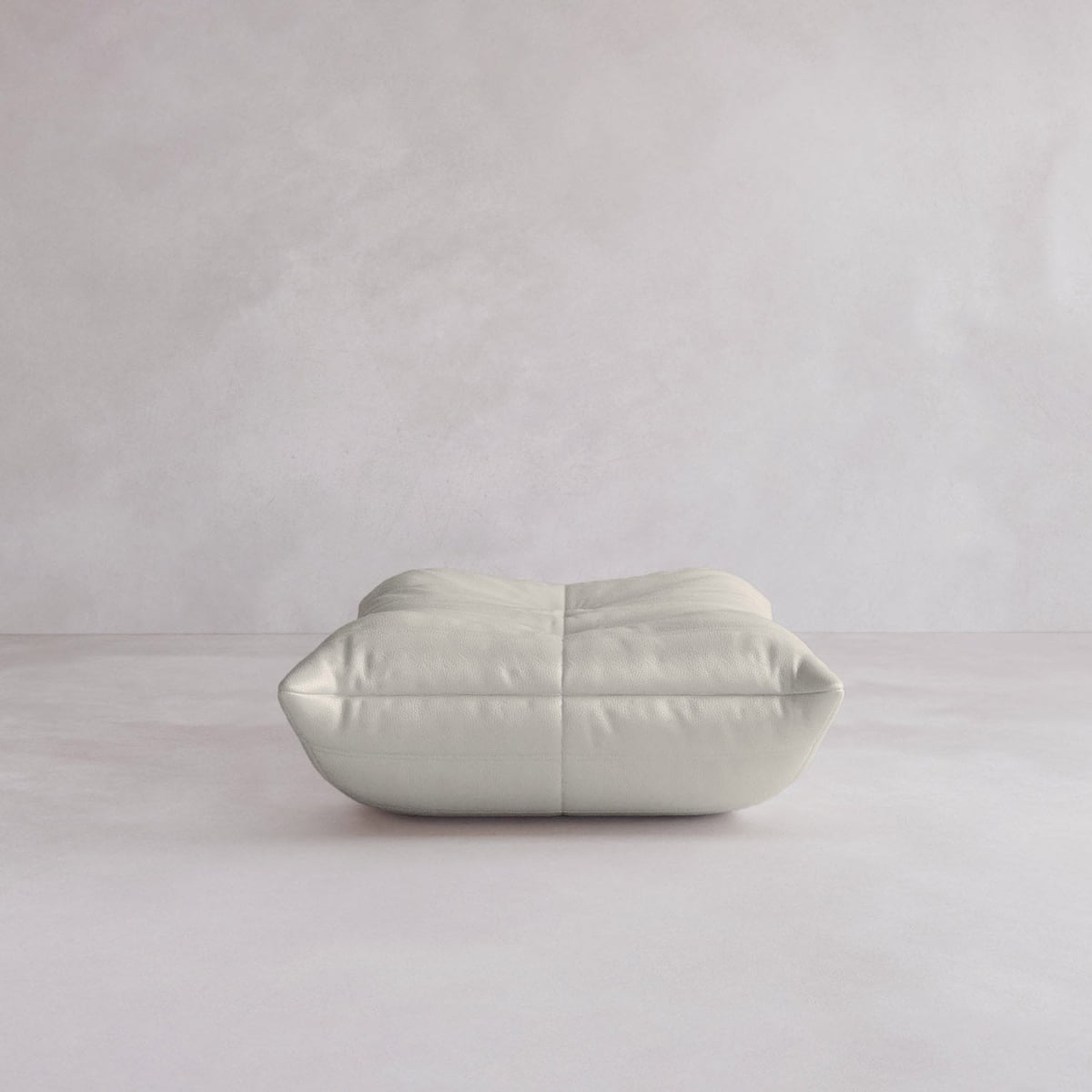 The Rolo Ottoman, a minimalist light grey floor cushion with a cushioned top, is centered on a smooth, pale floor against a soft, neutral wall.