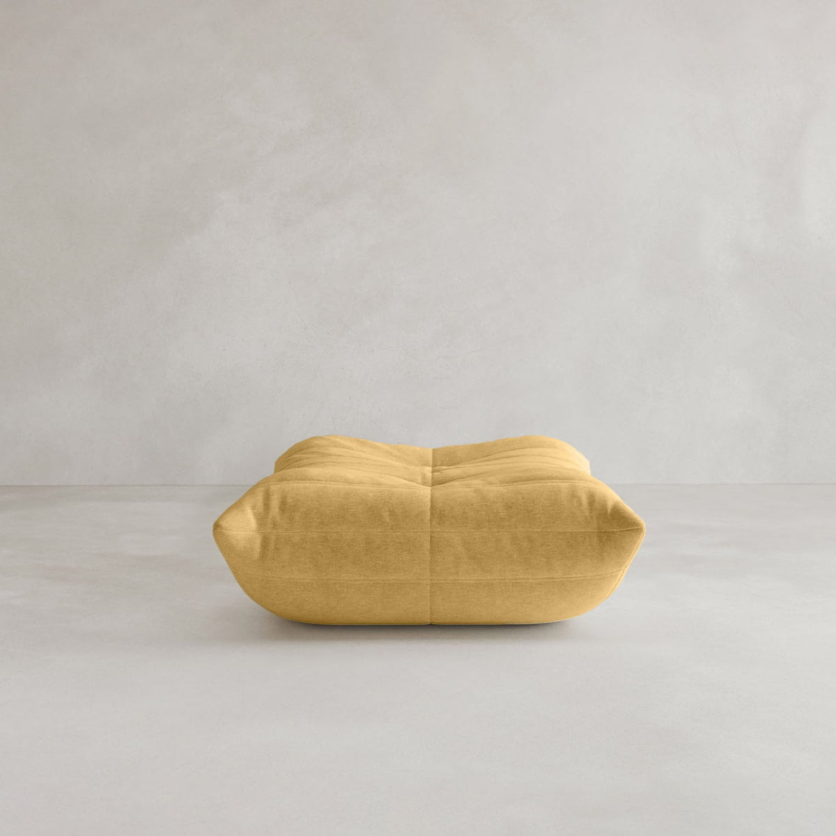 The Rolo Ottoman, a yellow, low rectangular floor cushion with a tufted top, sits on a smooth light gray floor against a pale wall—an invitingly versatile piece for any space.