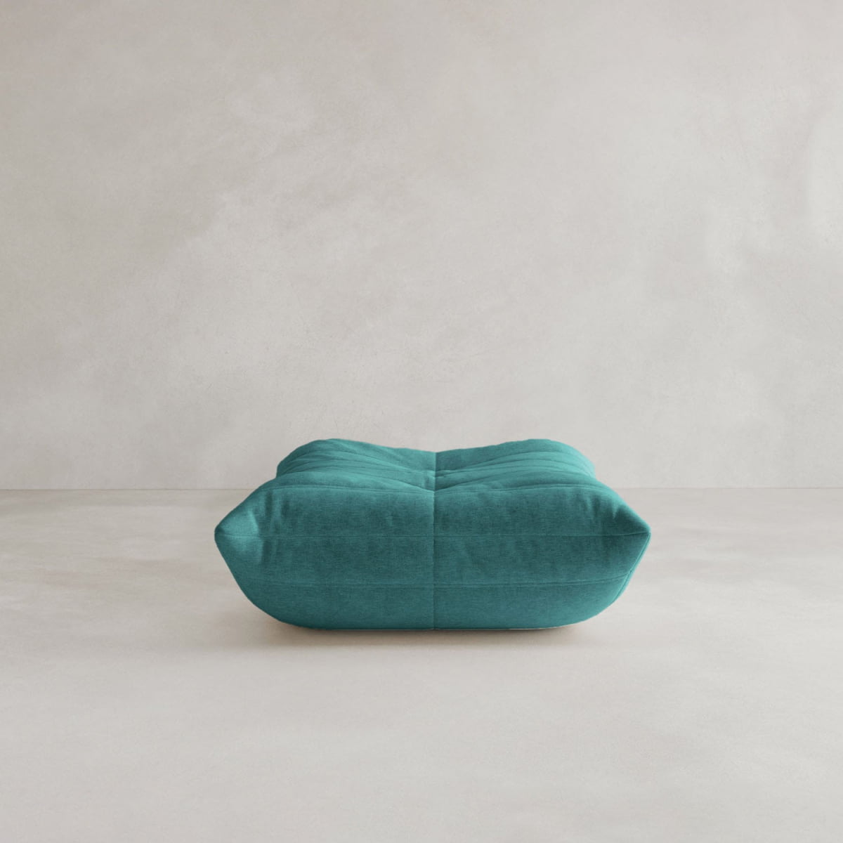 The Rolo Ottoman, in teal with a plush cushioned top and tufted details, sits on a light neutral floor against a plain wall, making it a versatile addition to any space.