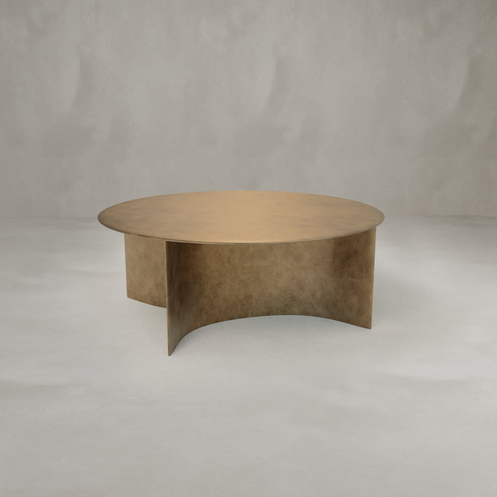 The Roma Coffee Table Large is a round, gold-colored table with an elegant flat top and intersecting curved base, making it a striking decor piece set against a plain, light gray background.