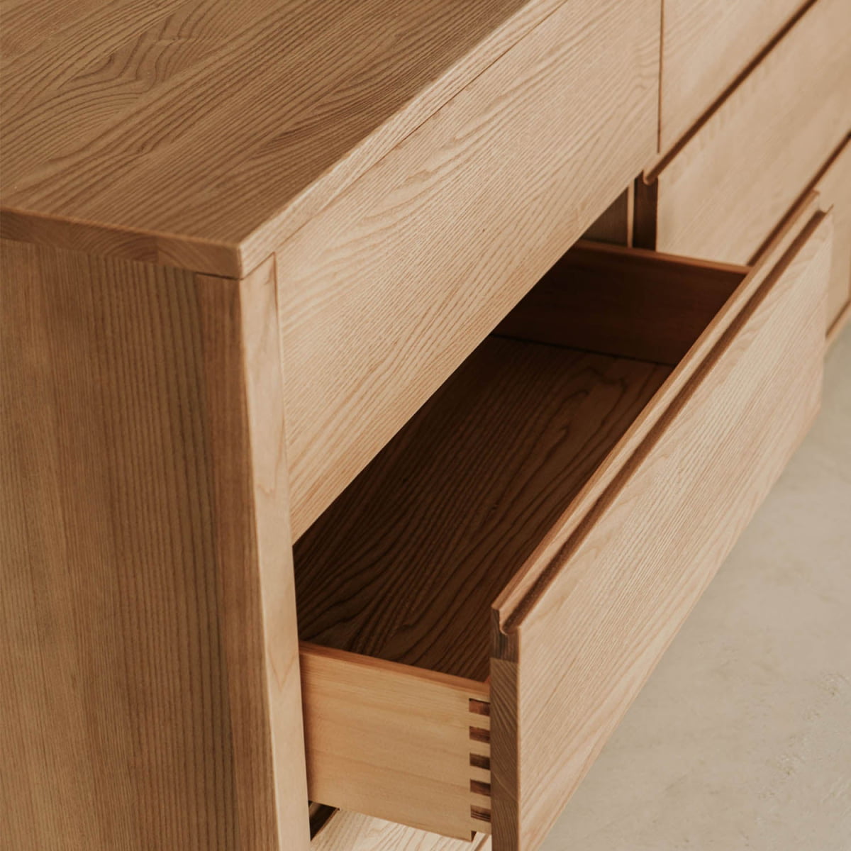 A close-up of the Sandringham Dresser with two drawers partially open highlights its natural wood grain and smooth finish—ideal storage for stylish bedrooms. The dresser is shown standing on a light-colored floor.