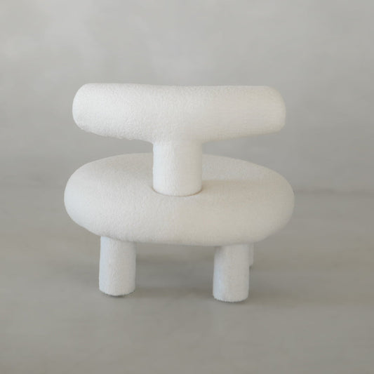 The Teddy Chair Rental features a modern, minimalist Neotenic design with a rounded seat, backrest, and thick cylindrical legs in soft textured fabric—a luxury statement piece set against a light gray background.