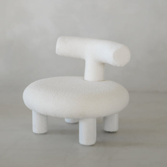 The Teddy Chair Rental is a modern, minimalist Neotenic chair with a round seat, cylindrical backrest, and four thick legs in soft white fabric—a luxury piece that makes a bold statement against a light grey background.