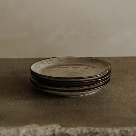A stack of four Tundra Glazed Dish Small plates sits on a textured stone surface, set against a softly lit, neutral background.