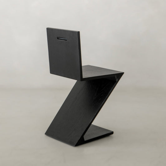 The Z Chair features a striking zigzag silhouette and a rectangular cutout near the top, making it an ideal choice for contemporary spaces with minimalist design against light, neutral backgrounds.