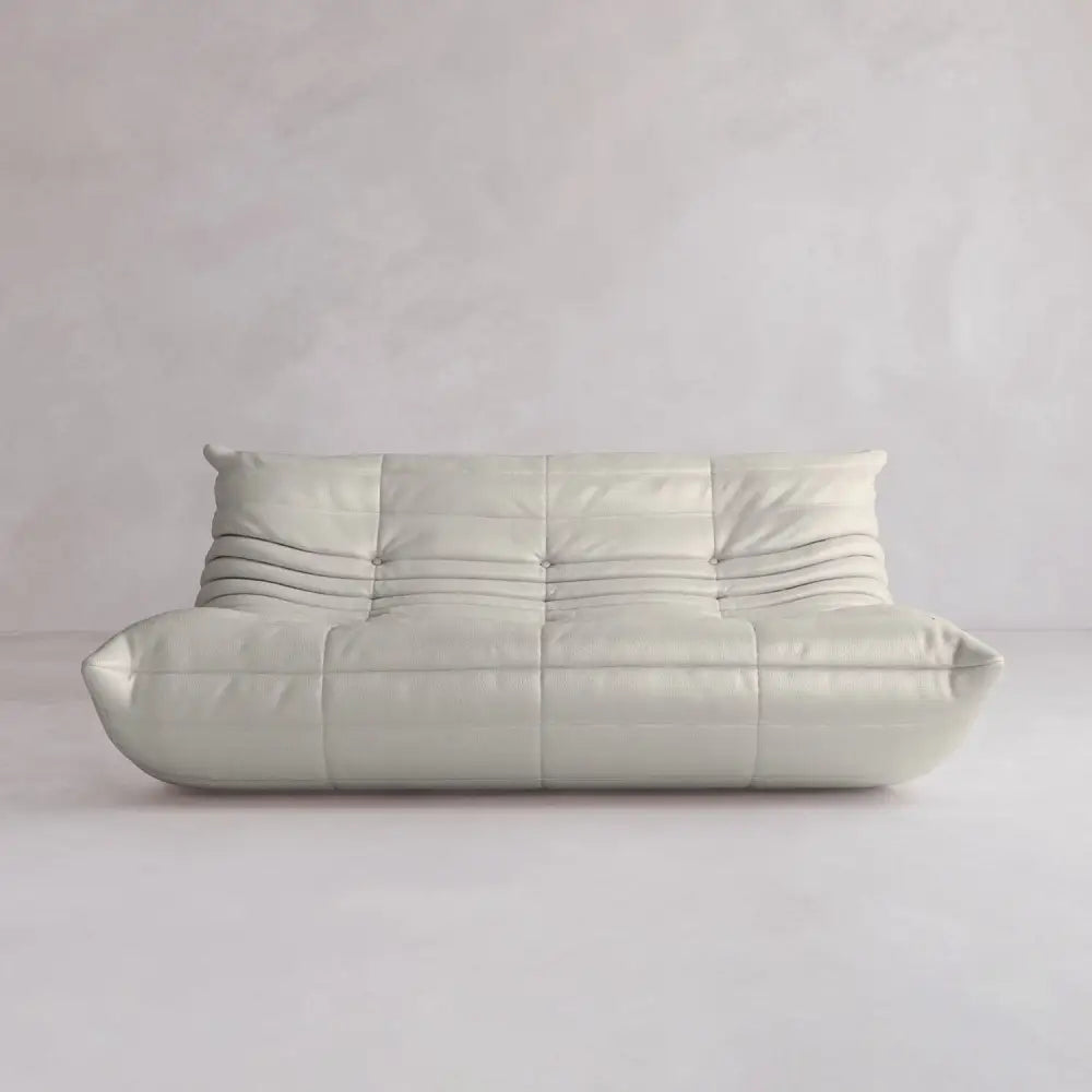 The Rolo Lounge Three Seater is a modern, low-profile off-white sofa with soft, rounded edges and horizontal seams, adding mid-century flair to any space with plain light walls and floors.