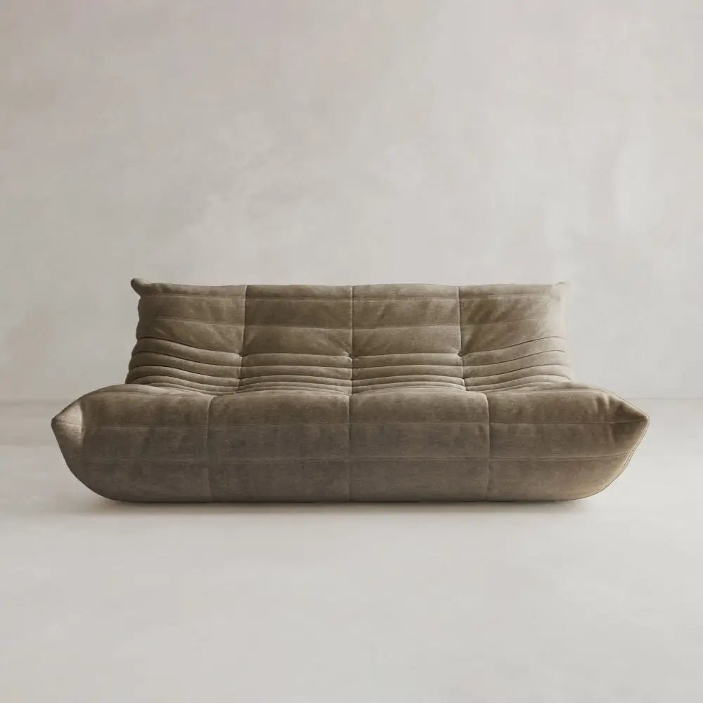The Rolo Lounge Three Seater is a modern, low-profile brown sofa with plush tufting and soft curves, inspired by mid-century design, shown against a plain light background.