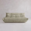 The Rolo Lounge Three Seater—a modern, light beige sofa with a low backrest, deep seat, and soft gathered upholstery inspired by mid-century design—sits against a plain, light-colored wall and floor.