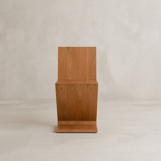 The Z Chair is a minimalist wooden chair with sharp, angular lines and a natural wood finish, perfect as an accent for contemporary interiors against a plain, light background.