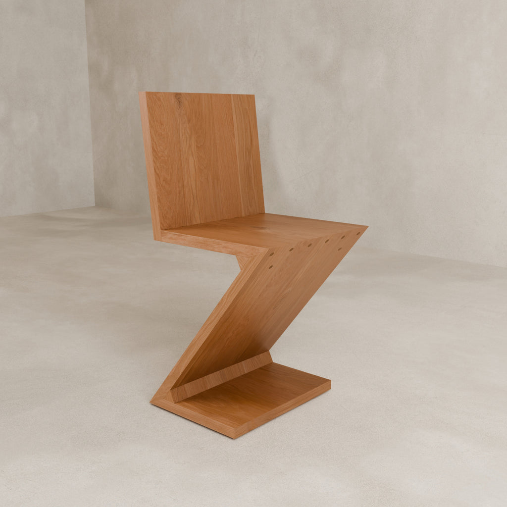 The Z Chair features a wooden build and angular, minimalist design, making it ideal for modern interiors. Placed on a light floor against a neutral wall, it complements any contemporary space.